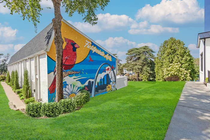 Vibrant apartment mural showcasing a red cardinal and city skyline under a bright blue sky, enhancing the lush green landscape of Fieldpointe Apartments.