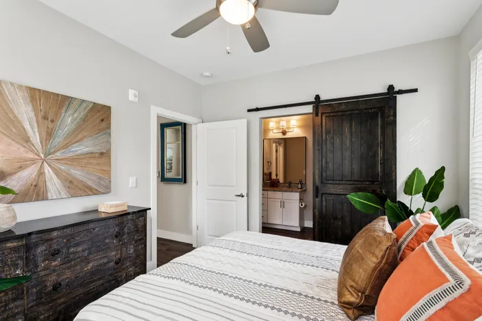 Chic bedroom with a rustic dresser, cozy patterned bedding, and a sleek barn door leading to the bathroom.