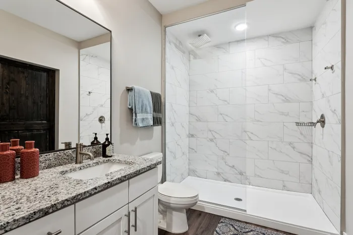 Elegant bathroom with a sleek marble shower, modern vanity with granite countertops, and warm lighting.