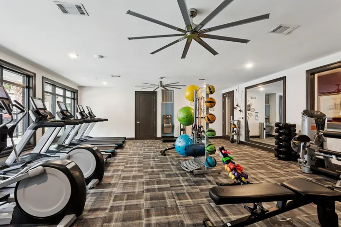 Modern fitness center with state-of-the-art equipment, including treadmills, ellipticals, and a variety of weights, set in a spacious, well-lit room with stylish flooring.