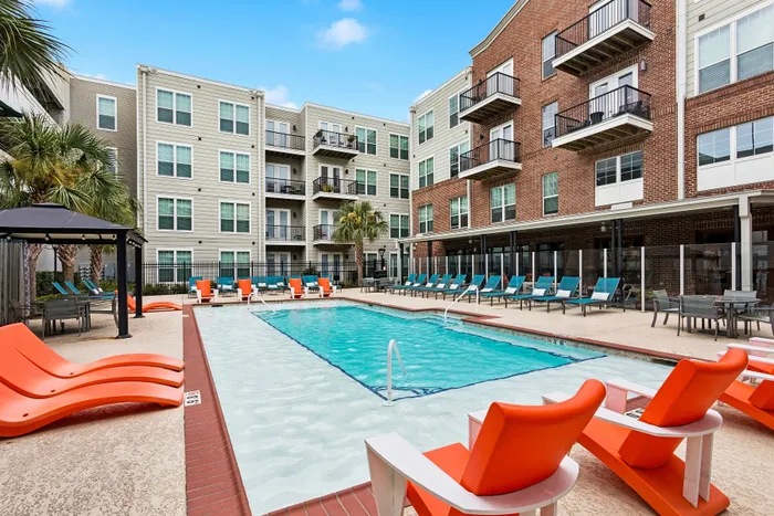 Modern apartment complex with a sparkling pool, vibrant orange loungers, and stylish balconies, offering a luxurious lifestyle.