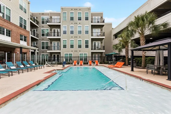 Modern apartment complex featuring a pristine swimming pool with stylish lounge chairs and lush palm trees, perfect for relaxation.