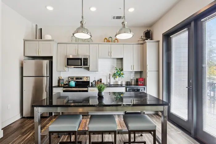 Modern kitchen featuring sleek stainless steel appliances, elegant cabinetry, stylish pendant lighting, and a spacious island with seating for three.