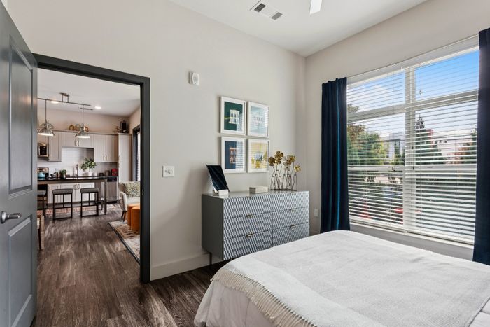 Bright bedroom with modern decor leading to a stylish, open kitchen with sleek cabinetry and ample natural light.