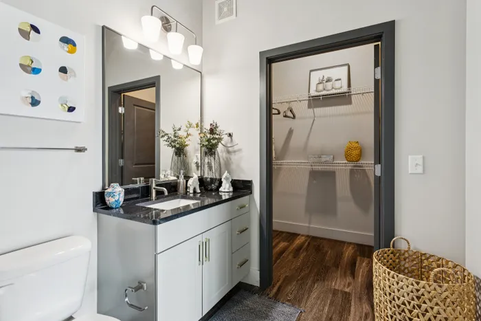 Contemporary bathroom featuring a sleek vanity with granite countertop, modern lighting, and a spacious walk-in closet with elegant decor.