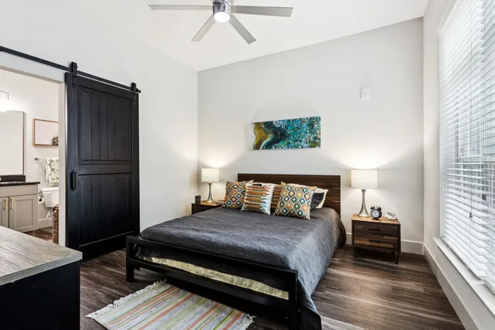 Modern bedroom with stylish decor, featuring a dark wooden bed, vibrant accent pillows, and a sliding barn door leading to an en-suite bathroom.