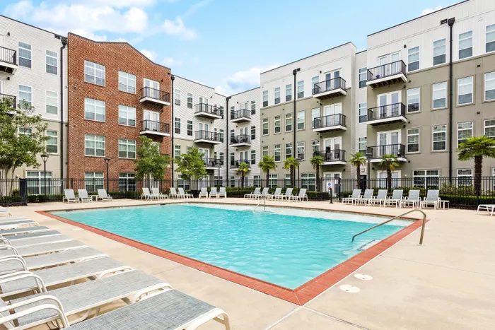 Modern apartment complex with a stunning outdoor pool, surrounded by palm trees and lounge chairs, offering a serene and luxurious living experience.