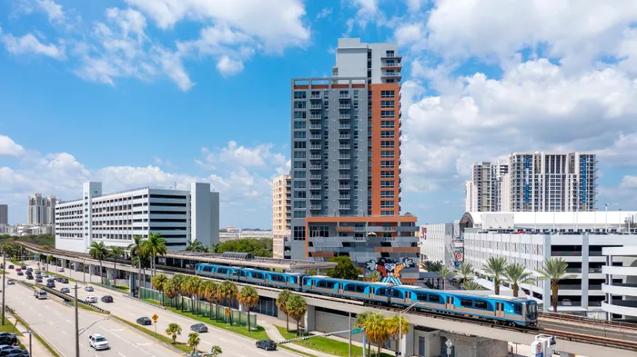 Vibrant urban scene showcasing a modern high-rise apartment building with a lively metro train passing by, set under a clear blue sky.