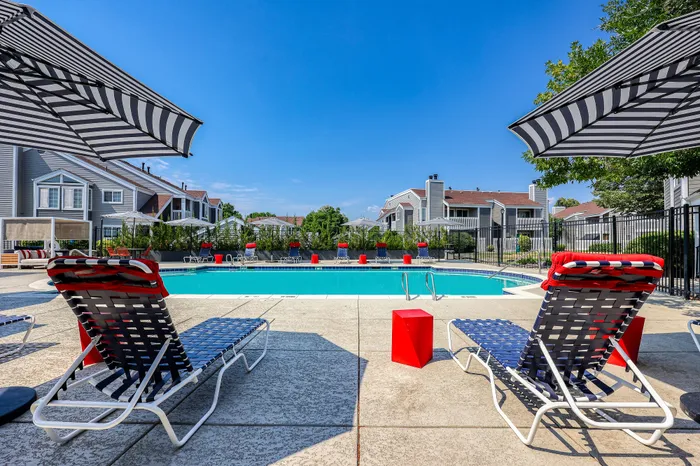 Luxurious apartment complex featuring a sparkling outdoor pool surrounded by stylish lounge chairs, perfect for relaxation under sunny blue skies.