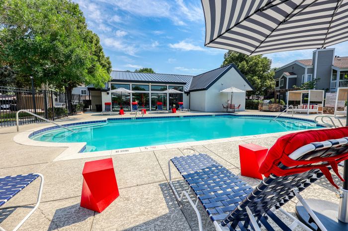 Inviting apartment community with a sparkling pool, lounge chairs, and modern sunshade, offering a perfect place to relax and unwind.