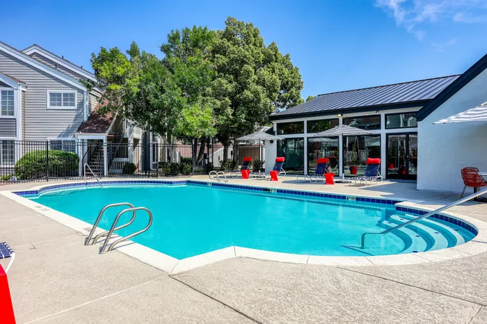 Inviting apartment complex pool area with stylish lounge chairs and vibrant umbrellas surrounded by well-maintained landscaping.