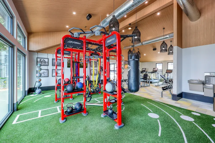 Modern gym with vibrant red exercise equipment, sleek design, large windows, and lush green AstroTurf flooring, perfect for dynamic workouts.
