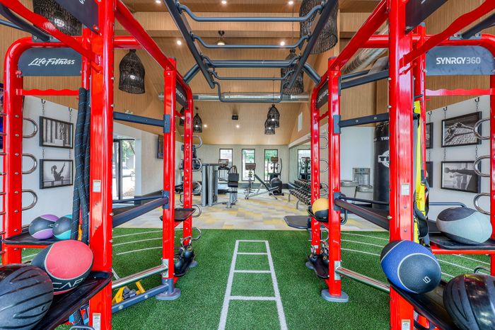 Modern gym facility featuring vibrant red fitness equipment, lush green turf flooring, and diverse workout stations for an invigorating exercise experience.