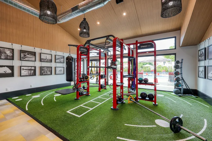 Modern fitness room with state-of-the-art equipment, vibrant green turf, and expansive windows with pool view.