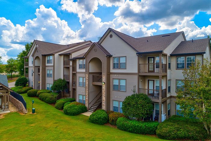 Charming three-story apartment complex with beautiful balconies, lush green landscaping, and picturesque clouds in the sky.