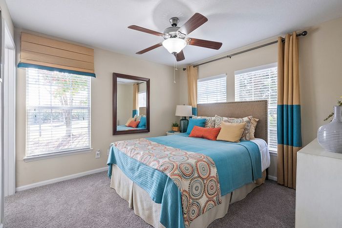 Bright and cozy bedroom with colorful bedding, large windows, and a modern ceiling fan, offering a welcoming atmosphere.