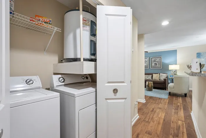 Inviting apartment showcasing an in-unit laundry area with washer and dryer, leading to a cozy living room with stylish decor and hardwood floors.