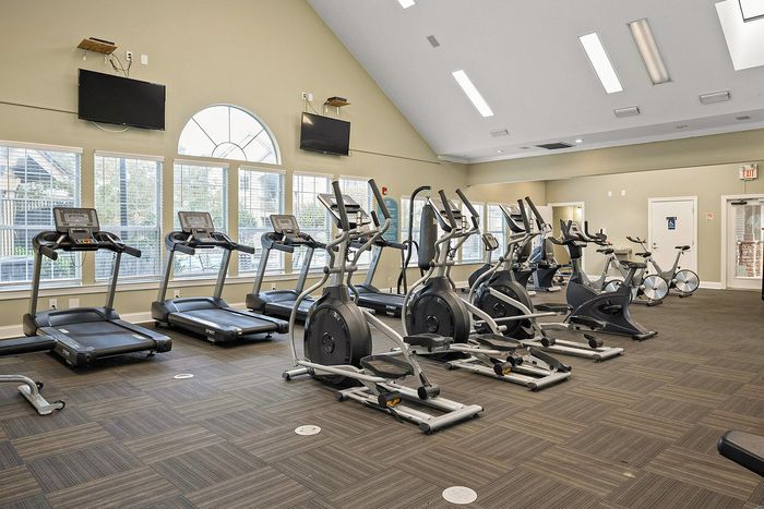 Spacious fitness center with modern treadmills, ellipticals, and bikes under high ceilings and abundant natural light.