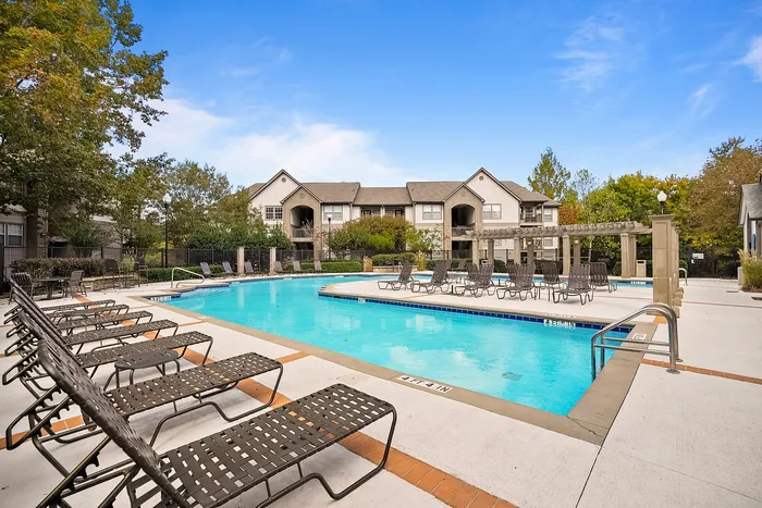 Inviting apartment complex with a pristine outdoor pool area surrounded by elegant lounge chairs and lush landscaping, perfect for relaxation.