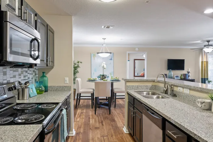 Modern kitchen with sleek appliances leading to a cozy dining area, featuring elegant decor and hardwood floors.