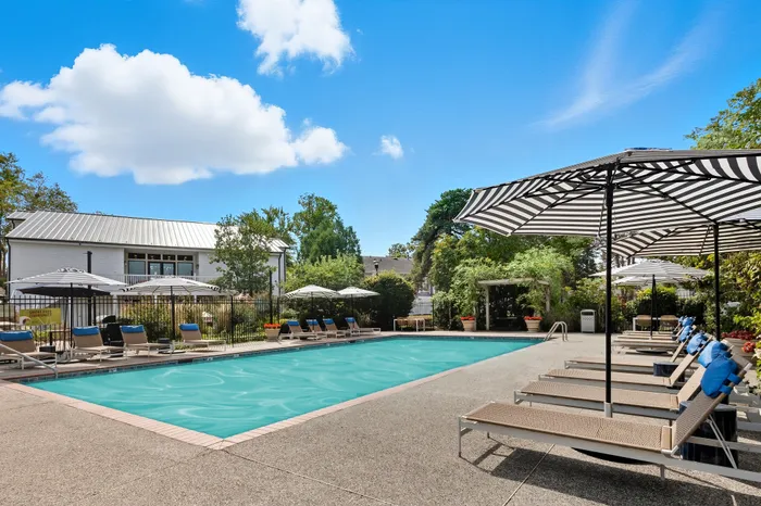 Luxurious outdoor pool area featuring stylish lounge chairs and striped umbrellas against a vibrant blue sky, perfect for relaxation and recreation.