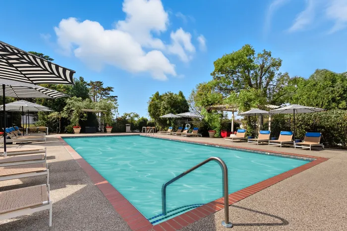 Inviting outdoor pool area with elegant lounge chairs, striped umbrellas, and lush green surroundings under a clear blue sky.