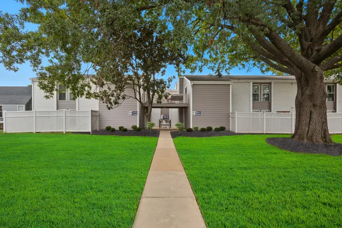Charming apartment building with manicured lawns, elegant white fencing, and mature trees, offering a serene residential ambiance.