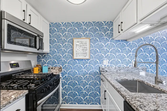 Chic kitchen with vibrant blue patterned wallpaper, stainless steel appliances, and granite countertops.