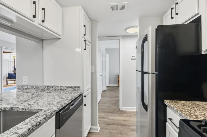 Elegant kitchen with sleek black appliances, modern cabinetry, and granite countertops. Bright open layout leading into a sunlit living area.