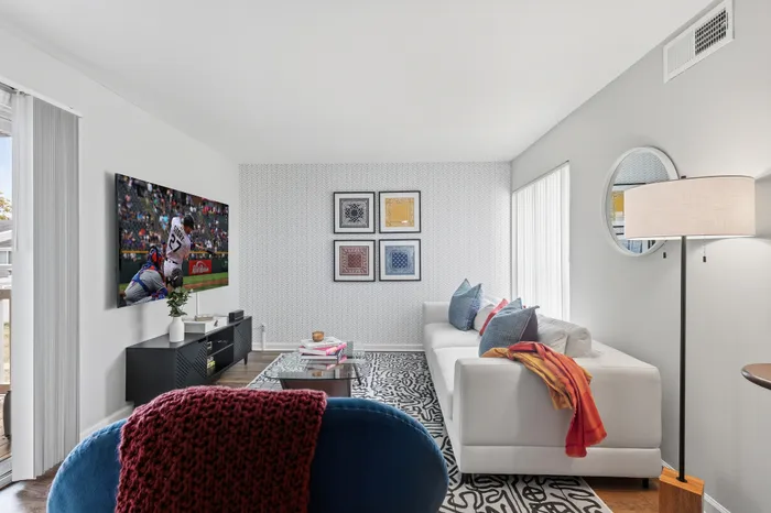 Modern living room featuring a cozy white sofa with colorful cushions, patterned area rug, and a stylish wall-mounted TV, perfect for relaxation and entertainment.