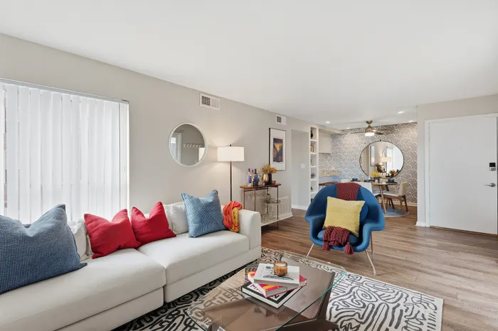 Bright and inviting living space featuring a stylish sofa with colorful pillows, sleek flooring, and a chic dining area with modern decor.