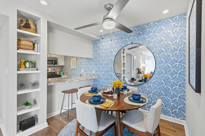 Chic dining area with a modern blue patterned accent wall, elegant round mirror, and cozy seating arrangement.