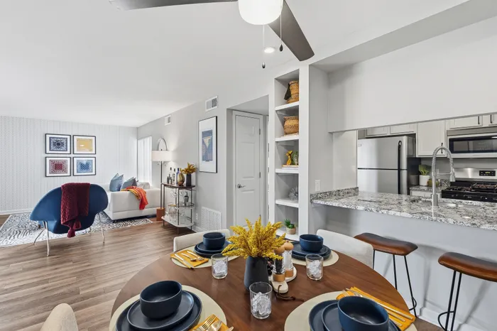 Modern open-plan living space featuring a stylish kitchen with granite countertops, cozy dining area set up with elegant dishware, and a chic living room with vibrant decor and ample natural light.