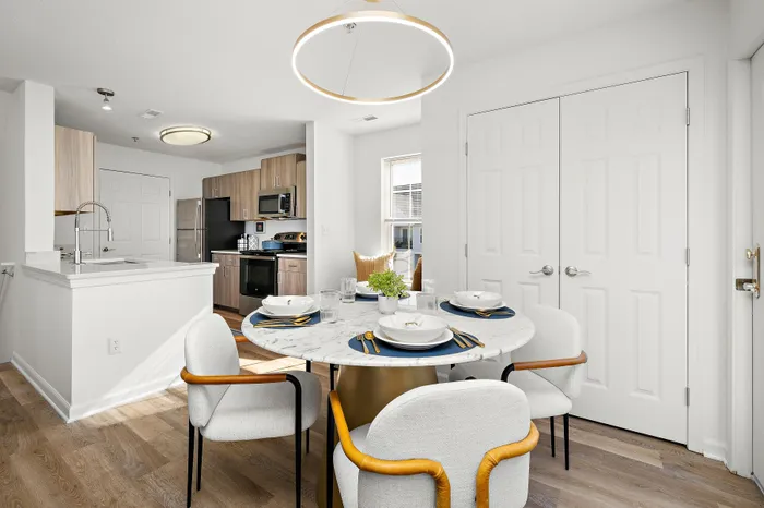 Bright and modern dining area with a marble table, surrounded by stylish chairs, adjacent to a sleek kitchen with stainless steel appliances.