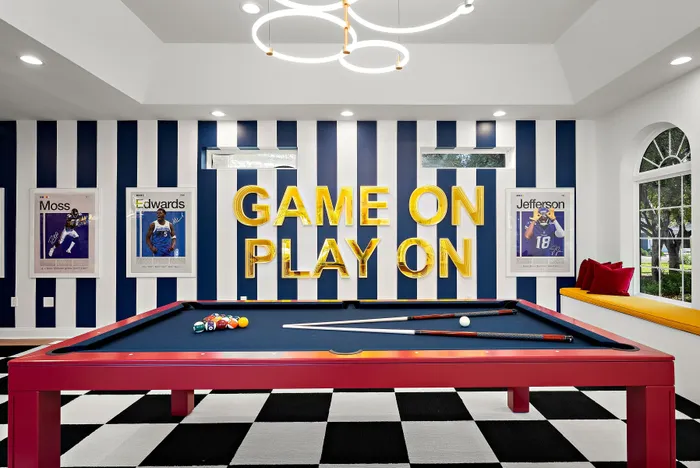 Vibrant game room featuring a sleek pool table, bold striped walls, modern lighting, and inspiring sports d&eacute;cor with 'Game On Play On' signage.