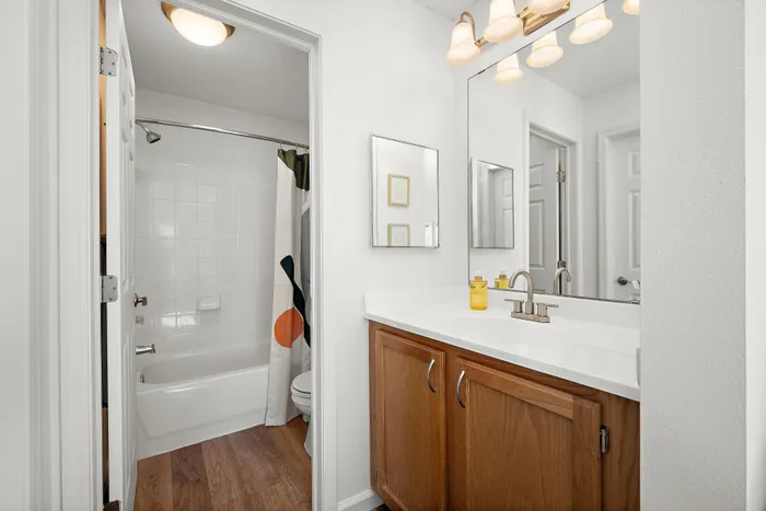 Elegant bathroom featuring a sleek vanity with large mirror, warm wood cabinetry, and inviting bathtub with stylish curtain.