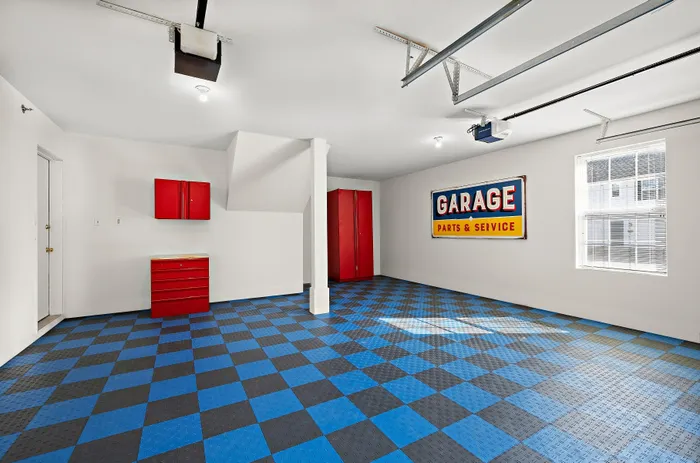 Spacious modern garage with vibrant blue and black checkered flooring, bright red storage cabinets, large window for natural light, and vintage garage sign providing a stylish touch.