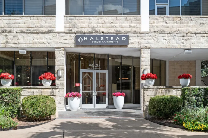Inviting entrance of a luxury apartment with elegant stone facade, large windows, and vibrant flower arrangements, exuding sophistication and style.