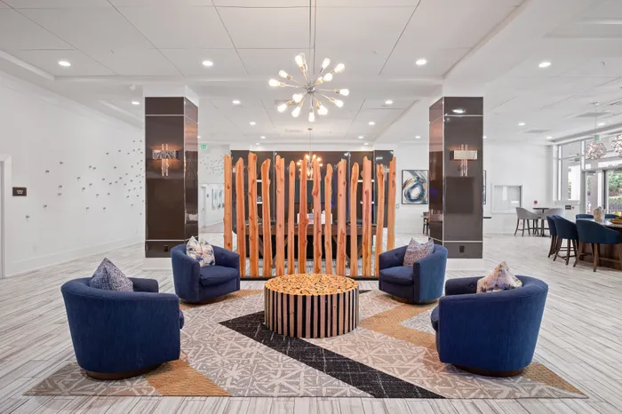 Elegant lounge area with modern blue chairs and a chic wooden centerpiece, illuminated by a trendy chandelier, perfect for relaxation and social gatherings.