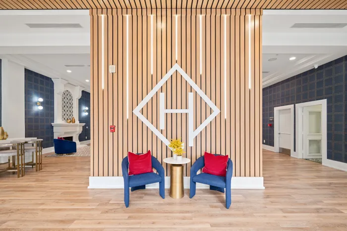Elegant apartment lobby with modern decor, featuring stylish wooden paneling, blue chairs with red cushions, and contemporary lighting.