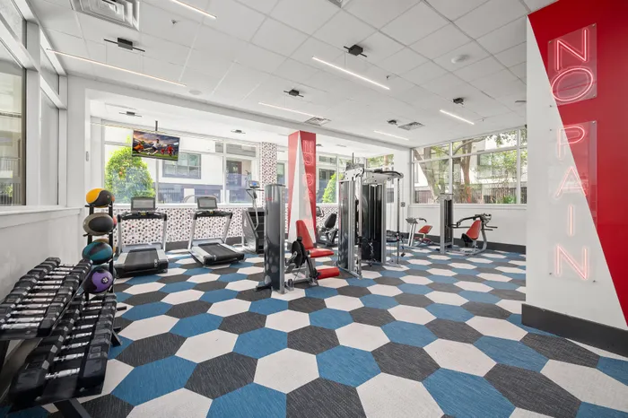 Modern gym with stylish hexagonal flooring, featuring state-of-the-art treadmills, weight racks, and fitness machines, illuminated by vibrant neon lighting.