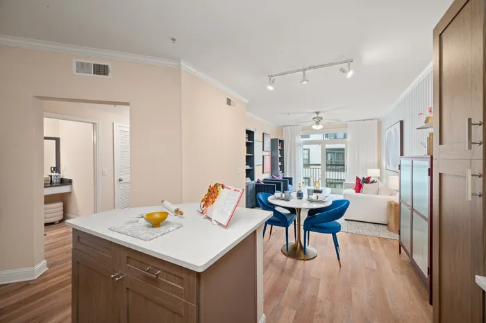 Modern open-concept apartment featuring a stylish kitchen island, elegant dining area with blue chairs, and bright living room with large windows.