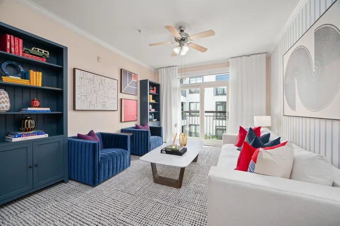 Modern living room with a chic design, featuring a plush white sofa, vibrant red and navy accents, stylish decor on navy bookshelves, and large windows for natural light.
