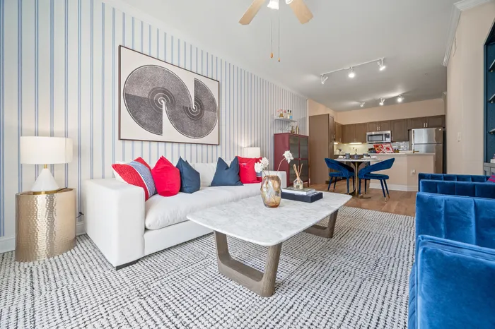 Chic and modern living room with stylish decor, plush white sofa, colorful cushions, and a sleek marble coffee table leading into an open-plan kitchen with elegant blue dining chairs.