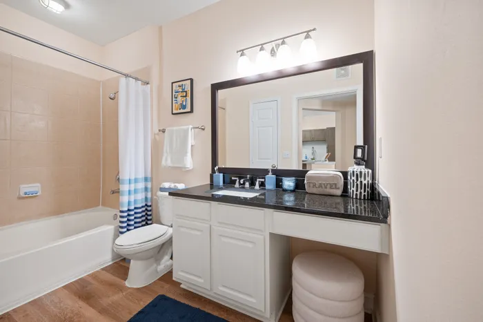 Elegant bathroom showcasing a modern vanity with a sleek, black countertop, ample storage, and bright lighting. Featuring a shower-tub combo with stylish tile walls and a chic blue-striped shower curtain, complete with soft lighting that enhances a relaxing ambiance.