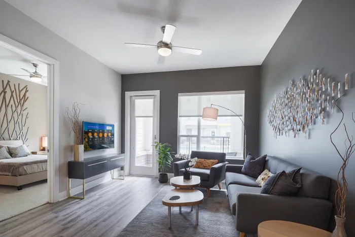 Dog-Friendly Apartments In Strip District, PA - Edge 1909 - A Modern, Moody Living Room With A Dark Grey Sofa, Charcoal Accent Wall, And A Large Metallic Branch-Like Wall Sculpture.