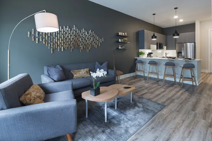 Contemporary living room with stylish decor, gray furniture, artistic wall design, and open-concept kitchen featuring modern amenities and bar seating.