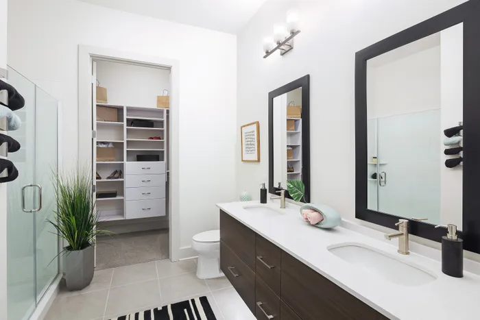 Modern bathroom with sleek double vanity, elegant mirrors, and spacious walk-in closet, creating a luxurious and organized space.