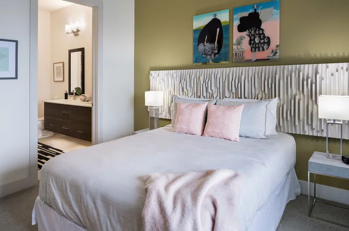 Elegant bedroom with modern decor, featuring a stylish green accent wall, unique wall art, and an en-suite bathroom with sleek fixtures.