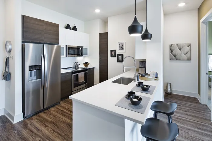 Strip District, PA, Luxury Apartments For Rent - Edge 1909 - A Modern Kitchen With A White Waterfall Peninsula, Dark Wood Lower Cabinets, White Upper Cabinets, And Black Pendant Lights.